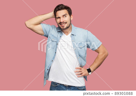 Portrait of query handsome bearded young man in blue casual style shirt standing and looking away and thinking what to do. indoor studio shot, isolated on pink background. Portrait of query handsome bearded young man in blue casual style shirt standing and looking away and thinking what to do. indoor studio shot, isolated on pink background. 89301088