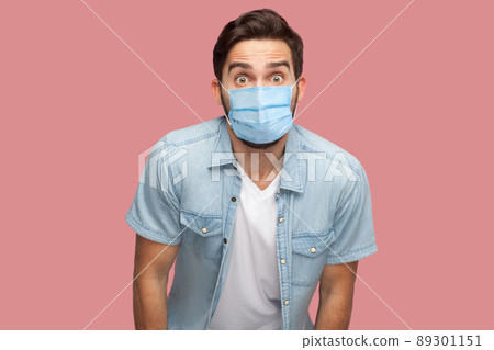Portrait of surprised young man with surgical medical mask in blue shirt standing and looking at camera with shocked unbelievable face. indoor studio shot, isolated on pink background. Portrait of surprised young man with surgical medical mask in blue shirt standing and looking at camera with shocked unbelievable face. indoor studio shot, isolated on pink background. 89301151