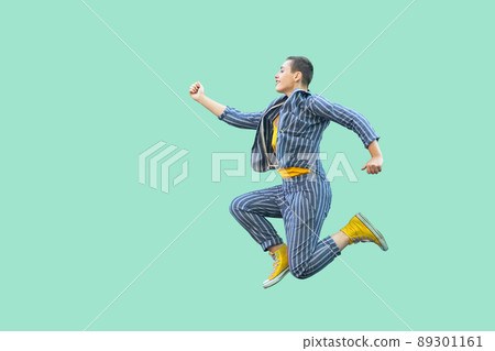 Profile side view portrait of happy handsome beautiful short hair young stylish woman in casual striped suit jumping in super mario pose. indoor studio shot isolated on light green background. 89301161