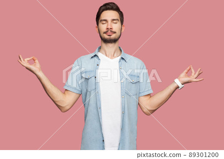 Portrait of calm relaxed handsome bearded young man in blue casual style shirt standing with raised arms and doing yoga meditating exercise. indoor studio shot, isolated on pink background. Portrait of calm relaxed handsome bearded young man in blue casual style shirt standing with raised arms and doing yoga meditating exercise. indoor studio shot, isolated on pink background. 89301200