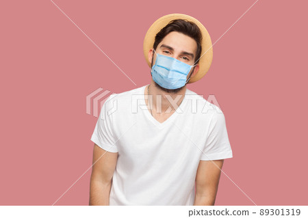 Portrait of happy young man with surgical medical mask in white shirt with hat standing and looking at camera with smile. indoor studio shot, isolated on pink background copyspace. Portrait of happy young man with surgical medical mask in white shirt with hat standing and looking at camera with smile. indoor studio shot, isolated on pink background copyspace. 89301319