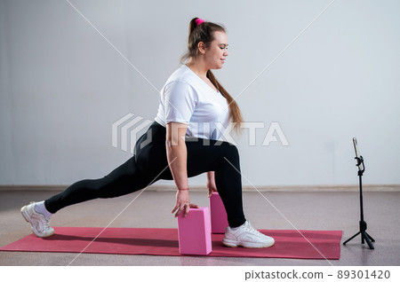 Young Plus Size Woman Stretching At Home Online. Flexible girl practices yoga and watches an online course on a laptop 89301420