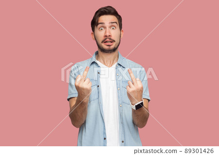 Portrait of angry handsome bearded young man in blue casual style shirt standing with middle finger fuck sign hand gesture and looking at camera. indoor studio shot, isolated on pink background. 89301426