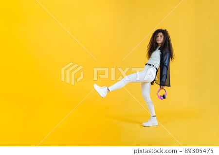 Young woman taking long step while walking in studio shot with yellow background Young woman taking long step while walking in studio shot with yellow background 89305475