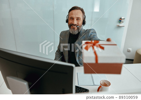 Smiling bearded man in headphones demonstrating a gift Smiling bearded man in headphones demonstrating a gift 89310059