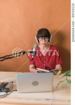 Portrait of mature woman wearing headphones and talking at online radio station - podcast and broadcast concept Portrait of mature woman wearing headphones and talking at online radio station - podcast and broadcast concept 89310119