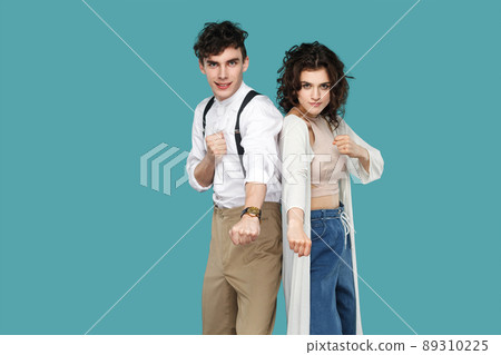 We are ready to ready to fight to win. Portrait of two funny brunette stylish partner standing with boxing fists and looking at camera with smile. indoor studio shot isolated on blue background. 89310225