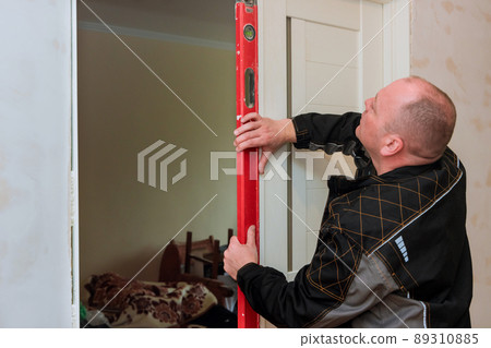 Carpenter worker installation process of checks level correctness installation wood door 89310885