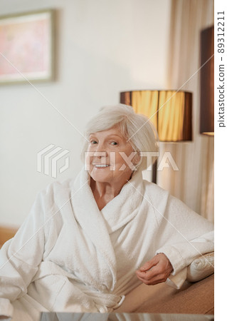 A good-looking old lady in a white robe in a hotel room A good-looking old lady in a white robe in a hotel room 89312211