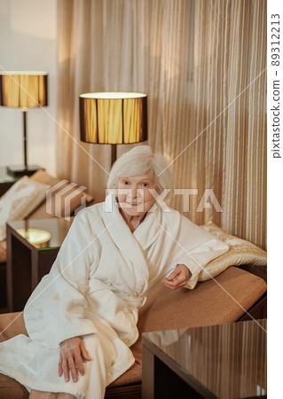 A good-looking old lady in a white robe in a hotel room A good-looking old lady in a white robe in a hotel room 89312213