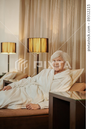 A good-looking old lady in a white robe in a hotel room A good-looking old lady in a white robe in a hotel room 89312215