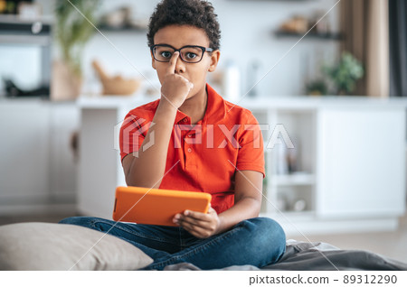 A boy in orange tshirt touching his eyewear and looking serious A boy in orange tshirt touching his eyewear and looking serious 89312290