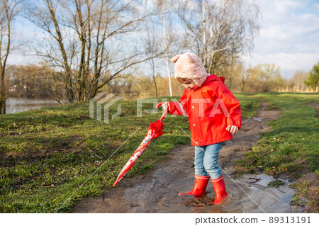 Child plays with umbrella after the rain in red rubber boots and a raincoat. 89313191