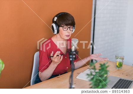 Portrait of mature woman wearing headphones and talking at online radio station - podcast and broadcast concept 89314363