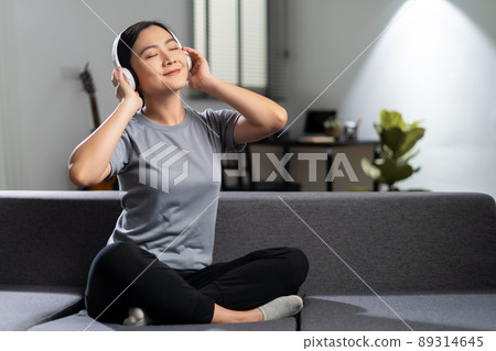 Happy woman with headphones and listening to music sitting on sofa at home. 89314645