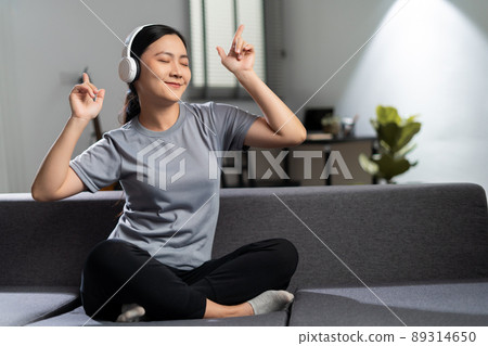 Happy woman with headphones and listening to music sitting on sofa at home. 89314650