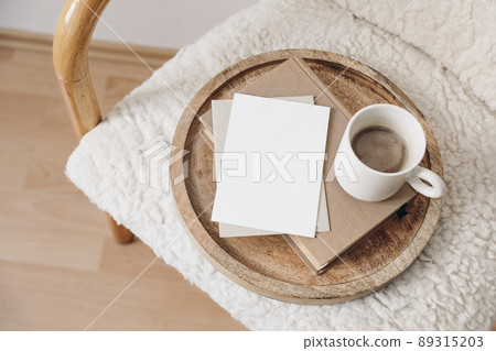 Boho breakfast still life scene. Blank greeting card, invitation. Book, cup of coffee. Wooden tray. Stationery mock-up. Elegant wooden chair, trendy wool teddy armchair, blurred beige floor. Flat lay Boho breakfast still life scene. Blank greeting card, invitation. Book, cup of coffee. Wooden tray. Stationery mock-up. Elegant wooden chair, trendy wool teddy armchair, blurred beige floor. Flat lay 89315203