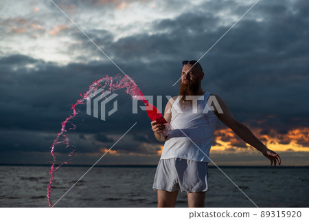 A humorous portrait of a brutal man pouring soda from a bottle on the beach at sunset A humorous portrait of a brutal man pouring soda from a bottle on the beach at sunset 89315920