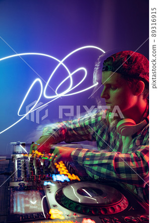 Portrait of young boy in casual cloth, party dj making music with professional sound mixer isolated over purple background in neon light 89316915