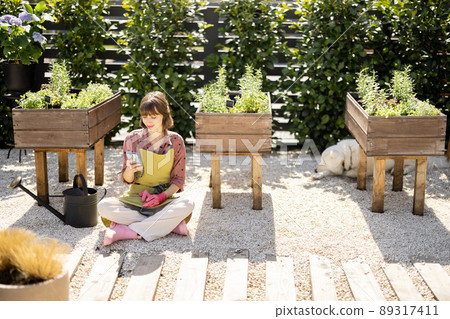 Woman using phone at home vegetable garden outdoors 89317411