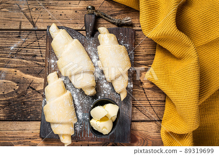 Raw uncooked french croissant on a wooden board. Wooden background. Top view 89319699