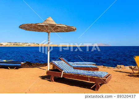 Sun umbrellas and chaise lounges on tropical beach. Concept of rest, relaxation, holidays, resort Sun umbrellas and chaise lounges on tropical beach. Concept of rest, relaxation, holidays, resort 89320437