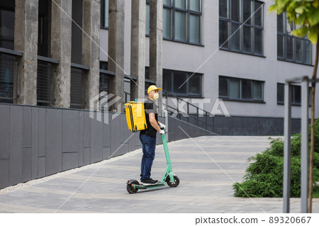Delivery man of takeaway in yollow face mask on scooter with isothermal food case box. Delivery man of takeaway in yollow face mask on scooter with isothermal food case box. 89320667