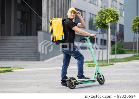 Delivery man deliver fresh hot food, rides fast on an electric scooter. Delivery man deliver fresh hot food, rides fast on an electric scooter. 89320684