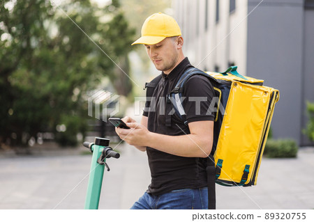 Courier man is looking in mobile phone to deliver address of food from a restaurant. Courier man is looking in mobile phone to deliver address of food from a restaurant. 89320755