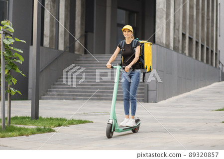 Delivery, woman with backpack riding scooter on city street. Delivery, woman with backpack riding scooter on city street. 89320857