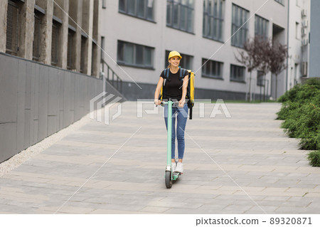 Delivery woman courier with isothermal backpack case rides her electric scooter 89320871