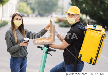 Pizza Delivery. Courier deliveryman in yellow uniform and face mask giving woman food order. Pizza Delivery. Courier deliveryman in yellow uniform and face mask giving woman food order. 89321689