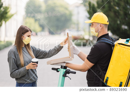 Pizza Delivery. Courier deliveryman in yellow uniform and face mask giving woman food order. Pizza Delivery. Courier deliveryman in yellow uniform and face mask giving woman food order. 89321690