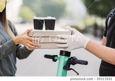 Courier delivering pizza boxes and two cups of coffee to caucasian girl customer in face mask. Courier delivering pizza boxes and two cups of coffee to caucasian girl customer in face mask. 89321692