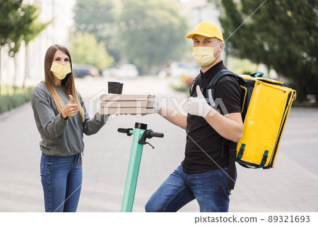 The girl takes pizza boxes and two cups of coffee from courier. The girl takes pizza boxes and two cups of coffee from courier. 89321693
