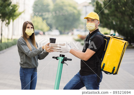 The girl takes pizza boxes and two cups of coffee from courier. The girl takes pizza boxes and two cups of coffee from courier. 89321694