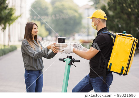 Attractive young delivery guy holding boxes with hot pizza and two cups of hot drink coffee. 89321696