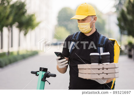 Courier delivering food and hot drinks outside. Guy using smartphone at city street. Courier delivering food and hot drinks outside. Guy using smartphone at city street. 89321697