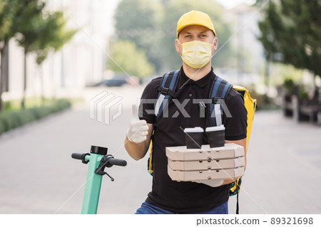Courier delivering food and hot drinks outside. Guy using smartphone at city street. Courier delivering food and hot drinks outside. Guy using smartphone at city street. 89321698