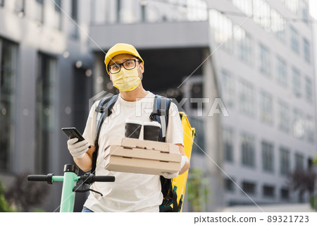 Delivery man in protective face mask holding stack of pizza cardboard boxes with two cups of coffee Delivery man in protective face mask holding stack of pizza cardboard boxes with two cups of coffee 89321723