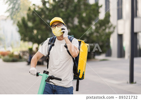 Delivery man in yellow uniform stands with smartphone against background of an apartment building Delivery man in yellow uniform stands with smartphone against background of an apartment building 89321732