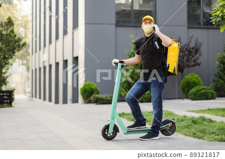 Delivery man in yellow uniform stands with a smartphone against the background Delivery man in yellow uniform stands with a smartphone against the background 89321817
