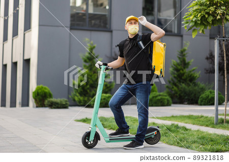 Courier deliver food on electric scooter wearing yellow facial protective mask Courier deliver food on electric scooter wearing yellow facial protective mask 89321818