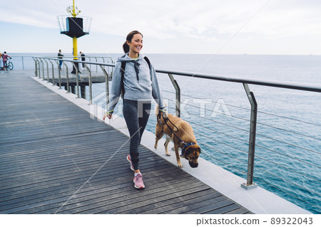 Active young woman with dog walking on promenade 89322043