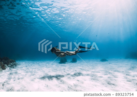 Attractive woman freediver with fins glides over sandy bottom. Freediving in ocean and sun rays 89323754