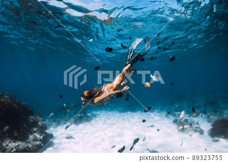 Beauty freediver lady with fins glides underwater with fishes in transparent ocean 89323755