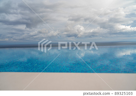 Infinity pool with sea and ocean views on the background of the sky with clouds. The clouds are reflected in the pool. 89325103