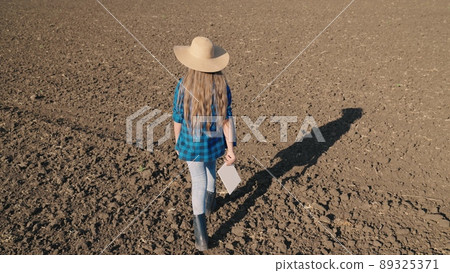 agriculture concept. farmer walks through field with digital tablet his hand. work plowed field. preparing field for planting seedlings. working man with digital tablet. agronomist rubber boots goes. agriculture concept. farmer walks through field with digital tablet his hand. work plowed field. preparing field for planting seedlings. working man with digital tablet. agronomist rubber boots goes. 89325371
