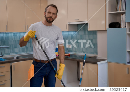 Young caucasian man in yellow rubber gloves holding mop Young caucasian man in yellow rubber gloves holding mop 89325417