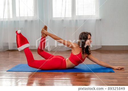 A beautiful sportive girl is engaged in yoga, pilates, exercises, body training. A woman in a red sports uniform against the background of the training hall. Healthy lifestyle concept. A beautiful sportive girl is engaged in yoga, pilates, exercises, body training. A woman in a red sports uniform against the background of the training hall. Healthy lifestyle concept. 89325849